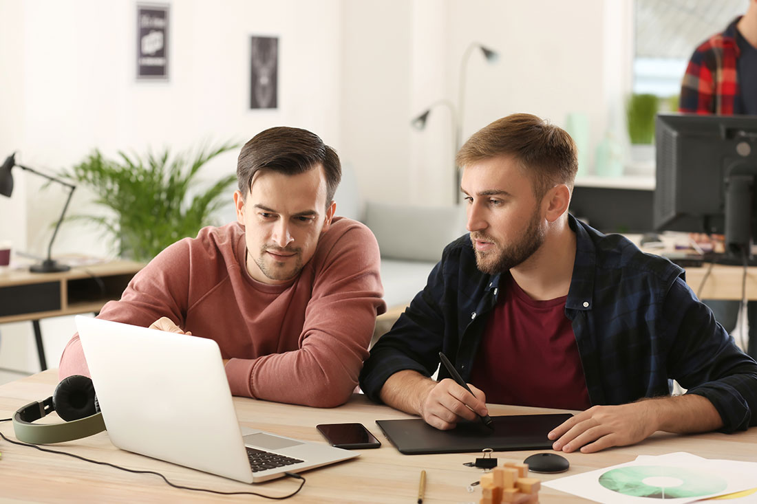two men working on laptop in an office setting