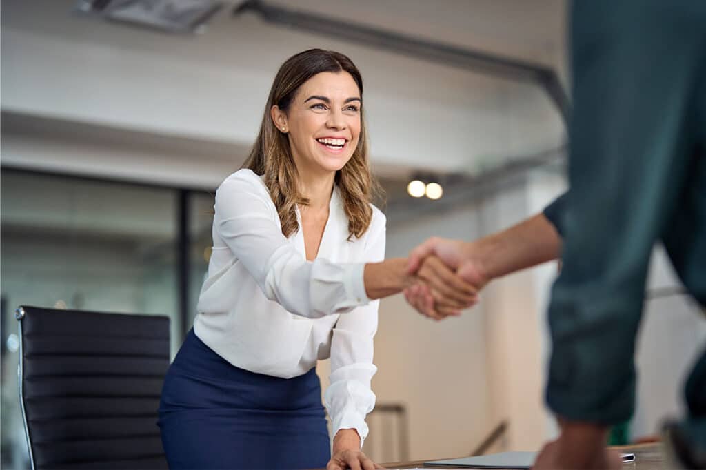 Happy mid aged business woman manager handshaking greeting client in office