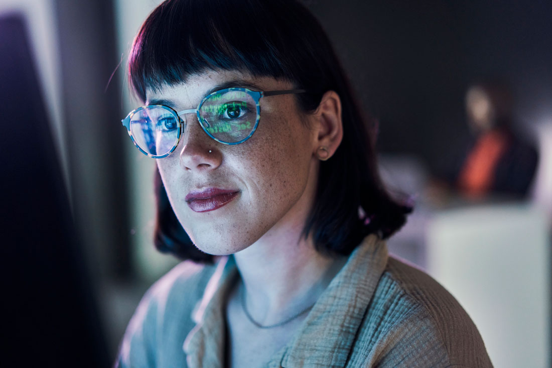 short-haired woman fixing AI bias with computer screen blue light reflecting in her glasses