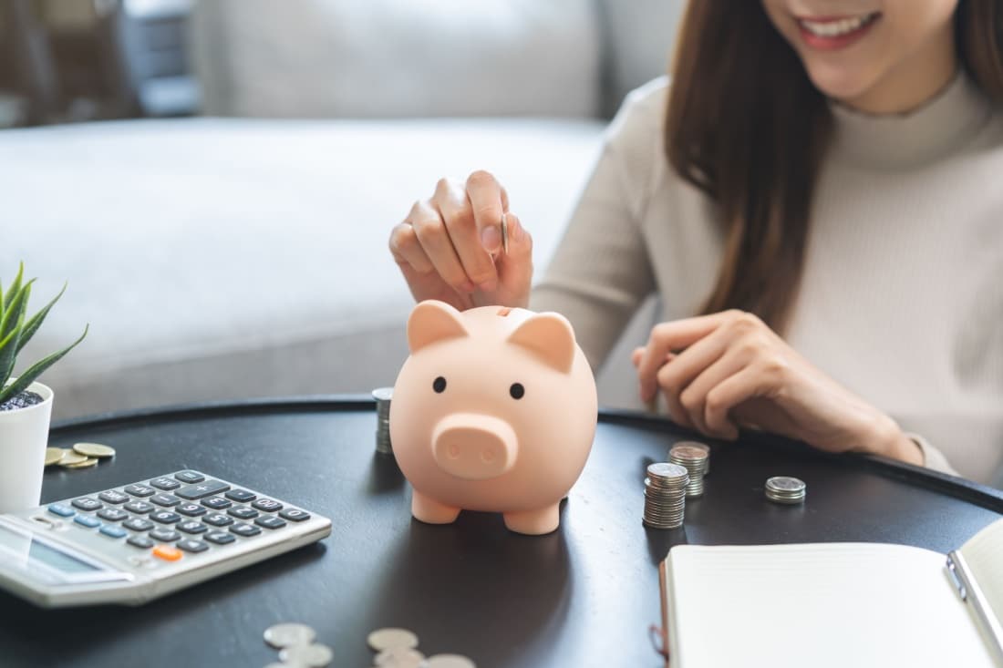 Close up shot of a woman's hands putting money in a piggy bank.