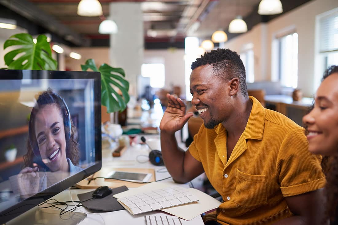 A Black man waves to his colleague on a video call from his office